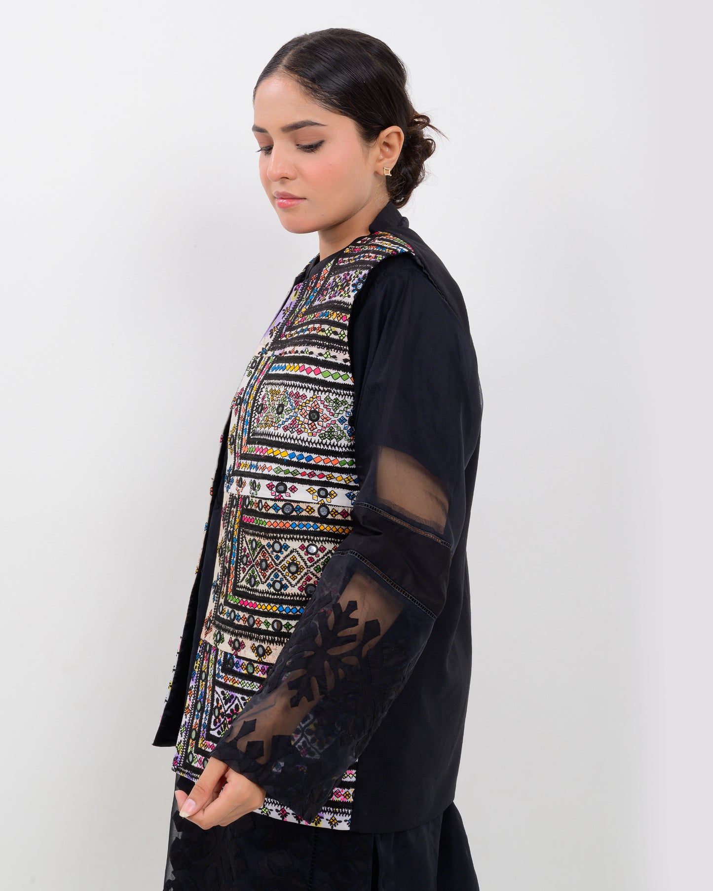 A woman wearing a colorful Balochi embroidered vest with sheer sleeves on a white background