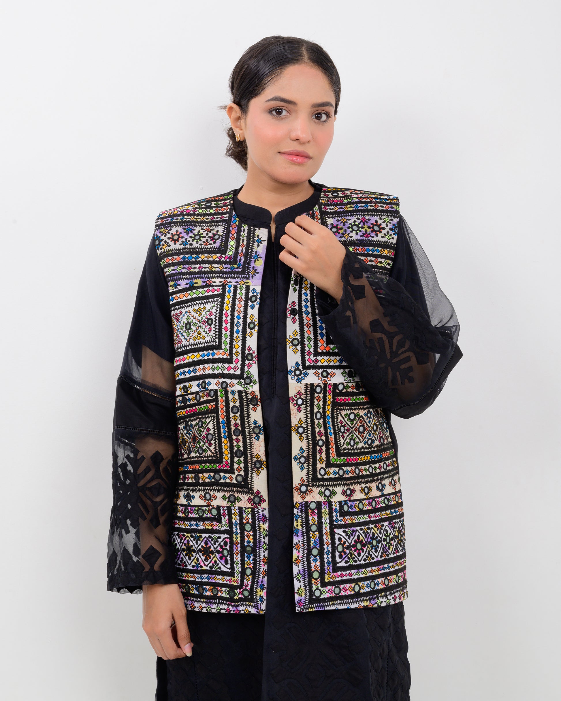 A woman wearing a colorful Balochi embroidered vest with sheer sleeves on a white background