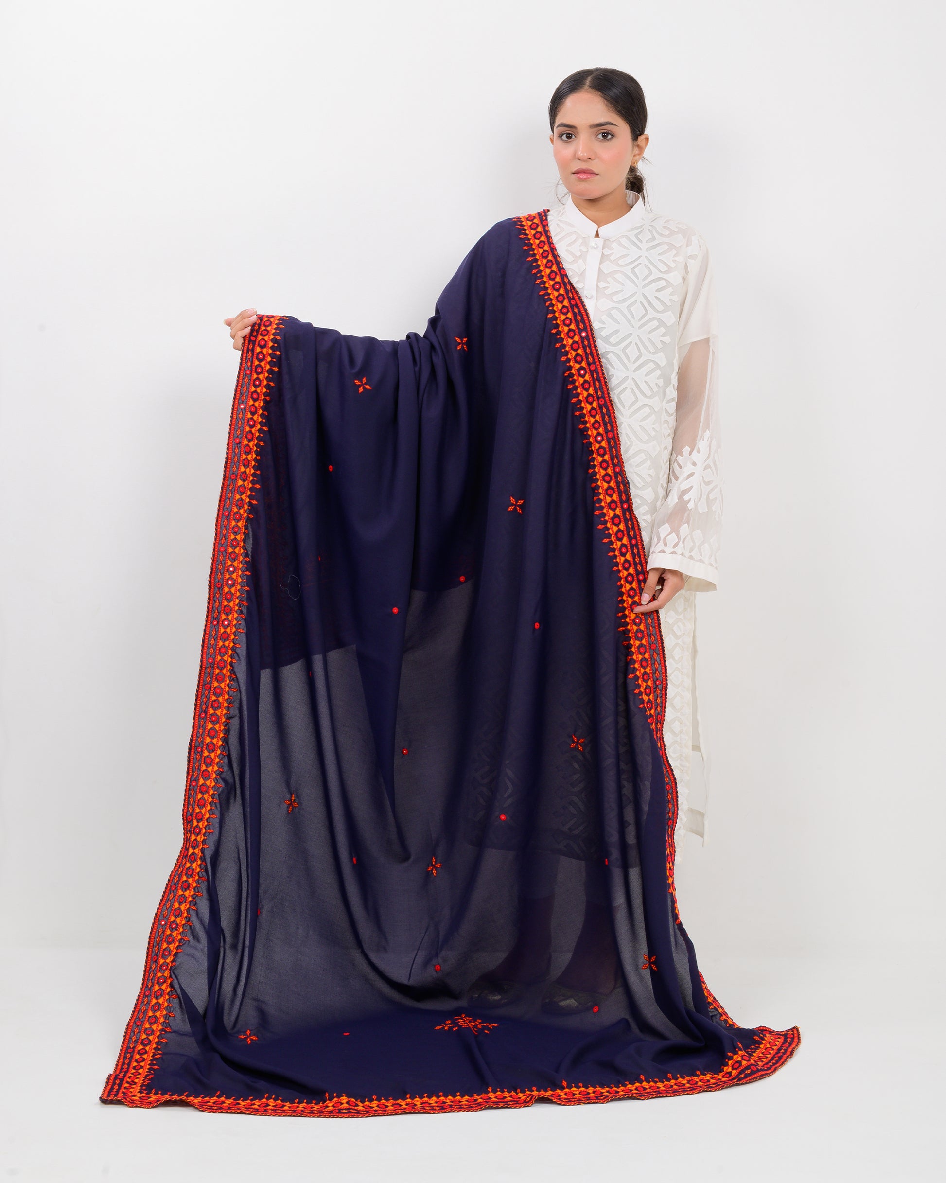 Woman wearing a navy blue shawl with orange embroidery on a white background