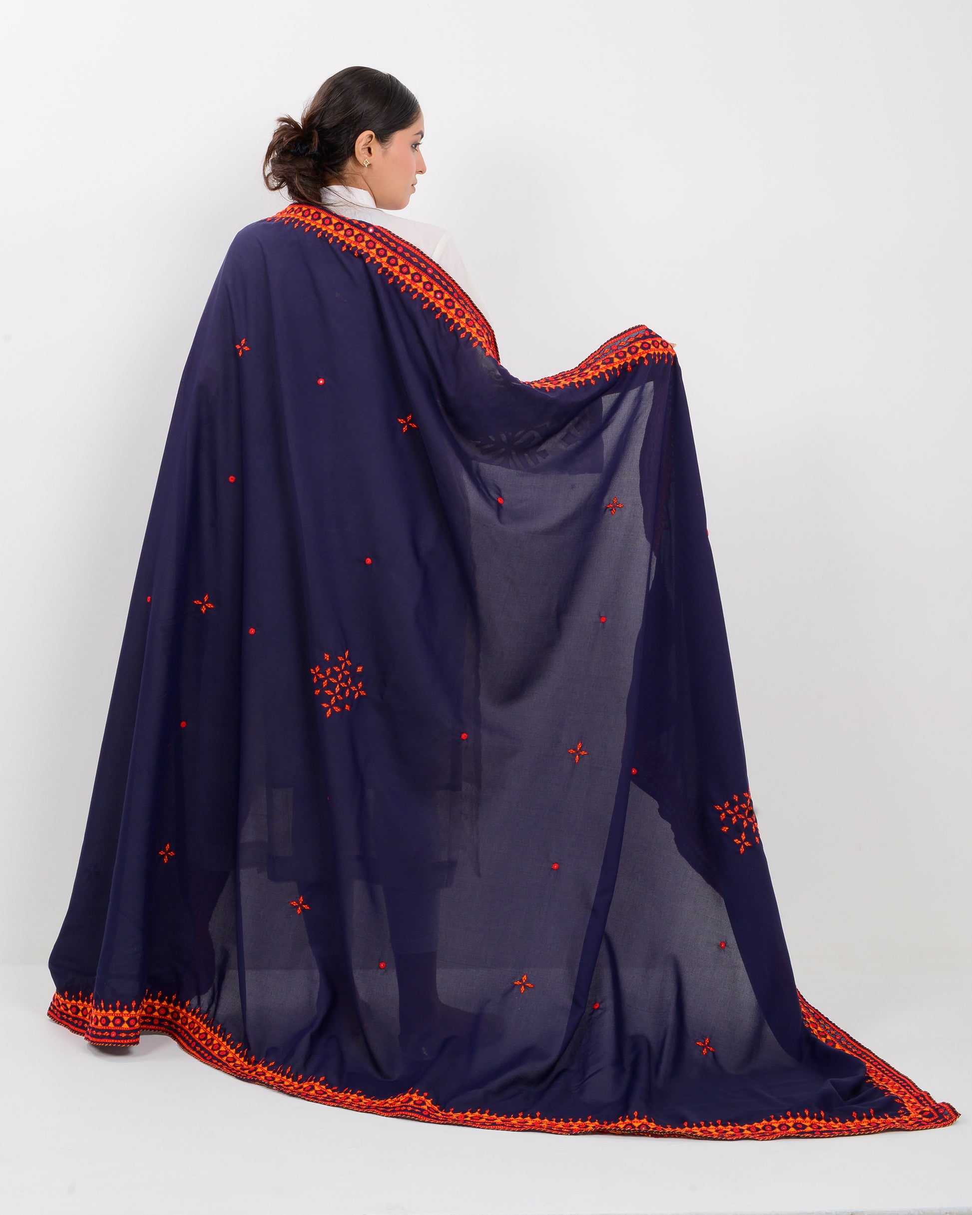 Woman wearing a navy blue shawl with orange embroidery on a white background
