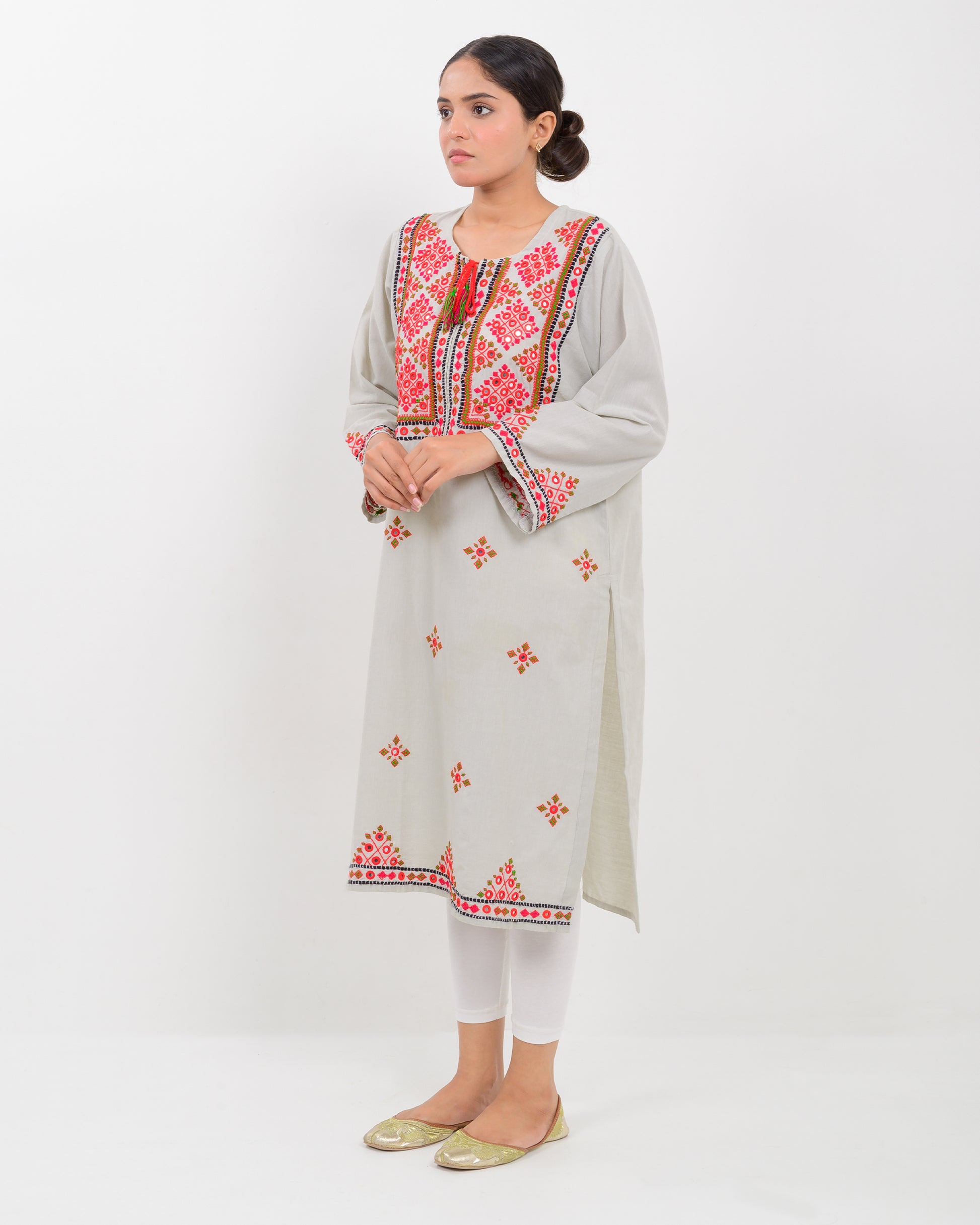 A woman wearing a light gray Balochi embroidery shirt on a white background