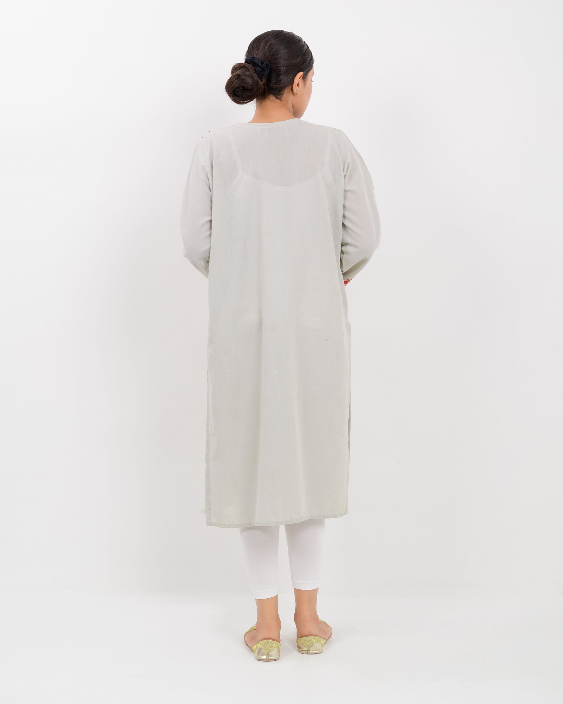A woman wearing a light gray Balochi embroidery shirt on a white background