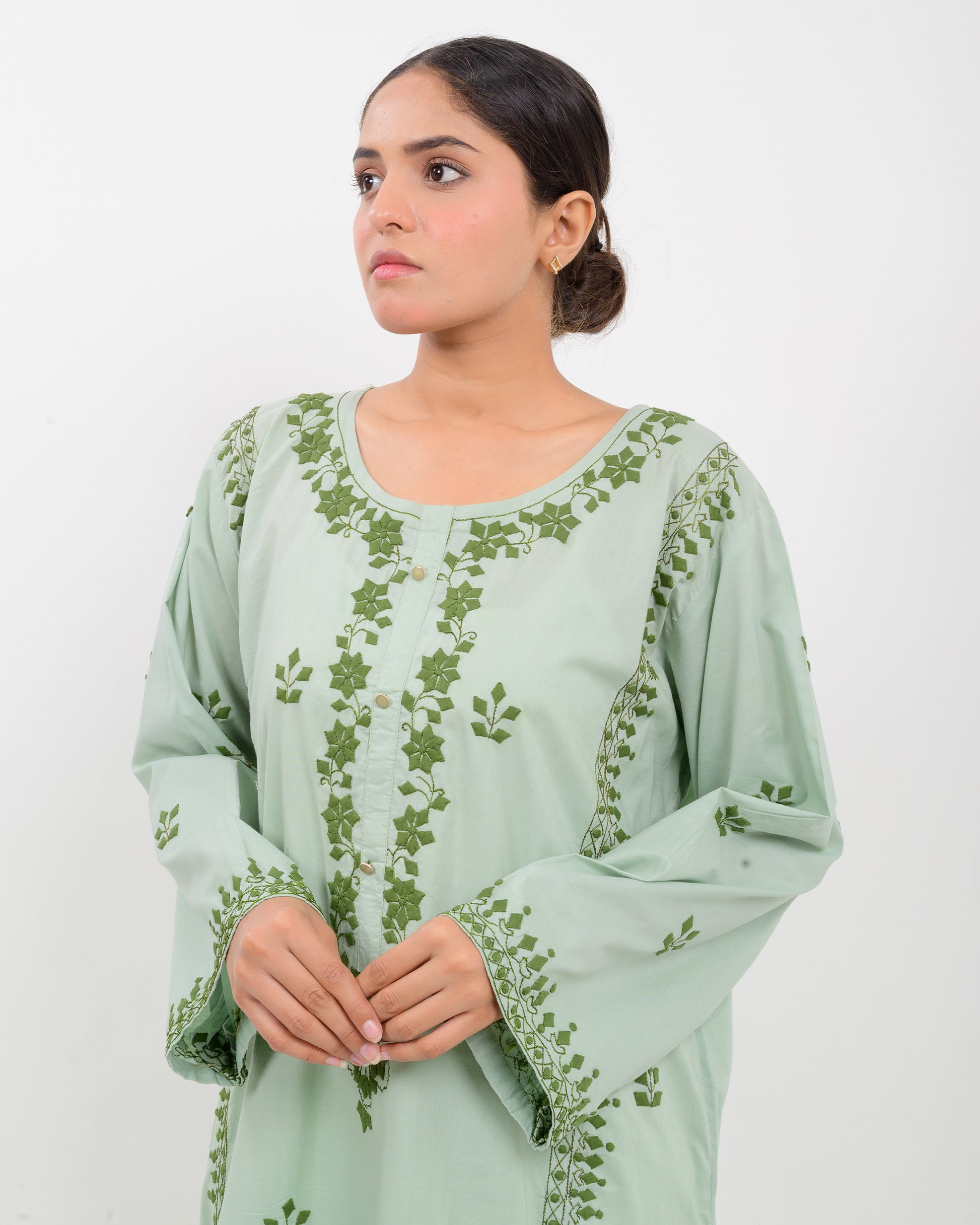 Woman wearing an Applique cutwork green embroidered Shirt with white pants on a white background