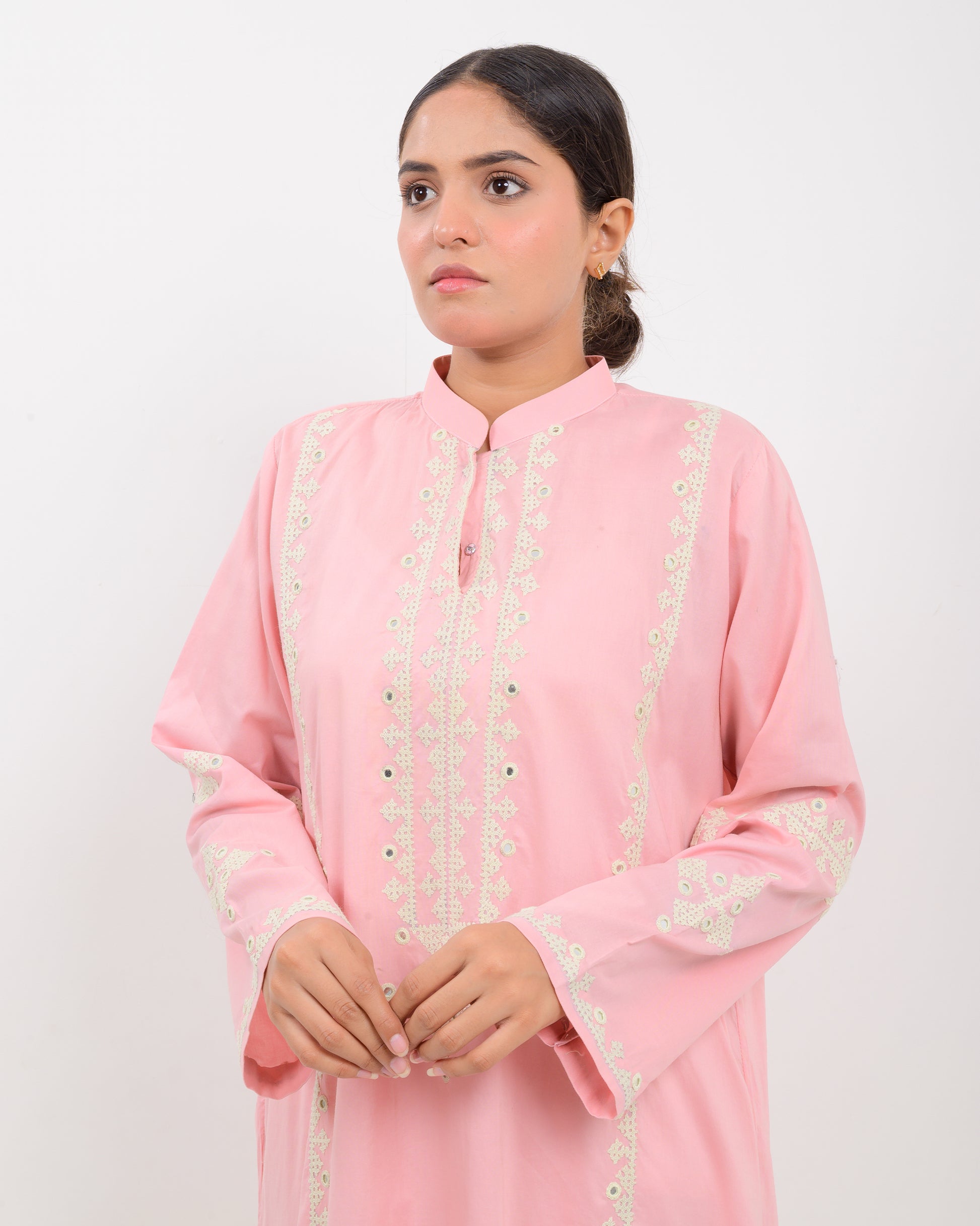 Woman wearing a pink cotton shirt with white embroidery on a white plan background