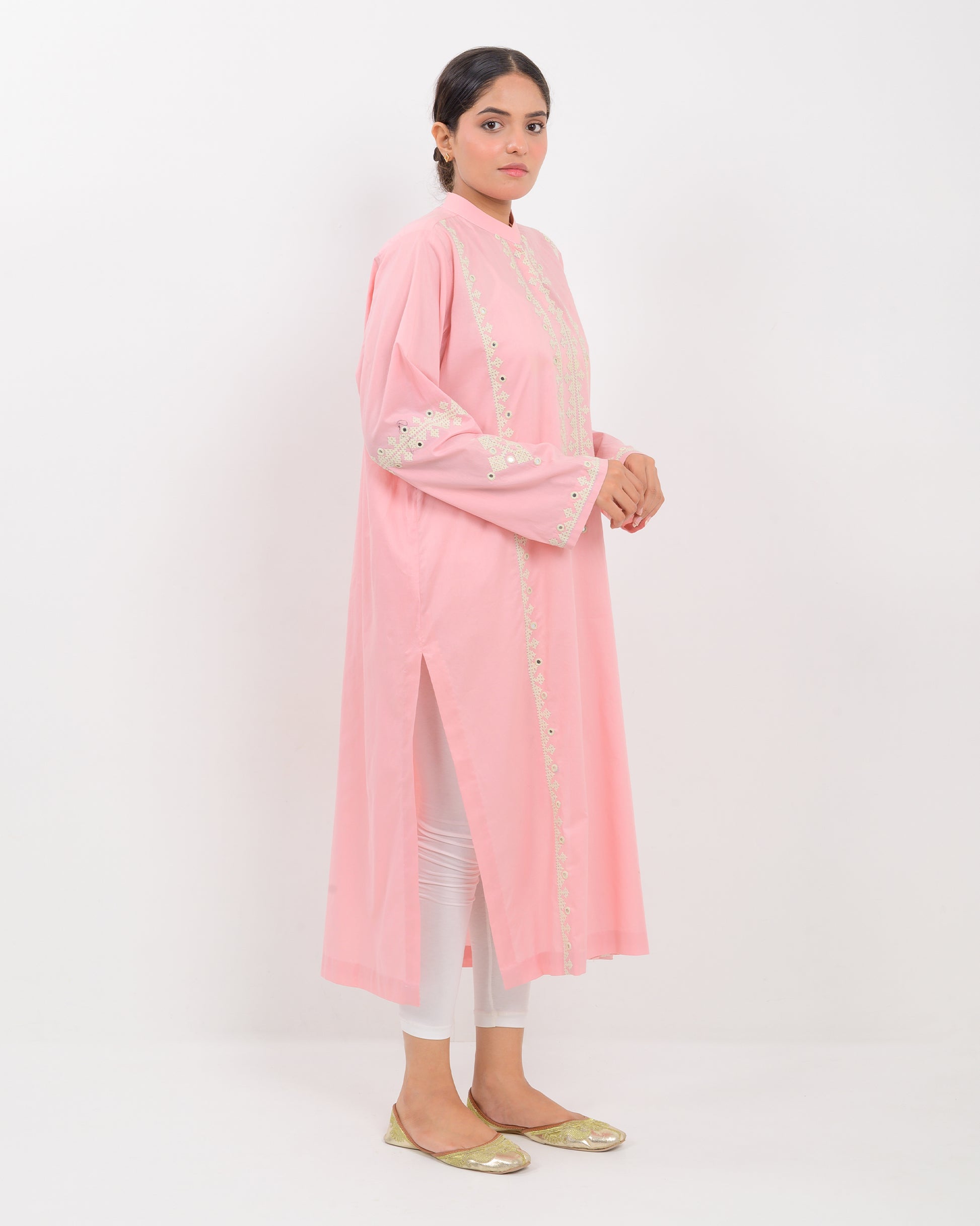 Woman wearing a pink cotton shirt with white embroidery on a white plan background