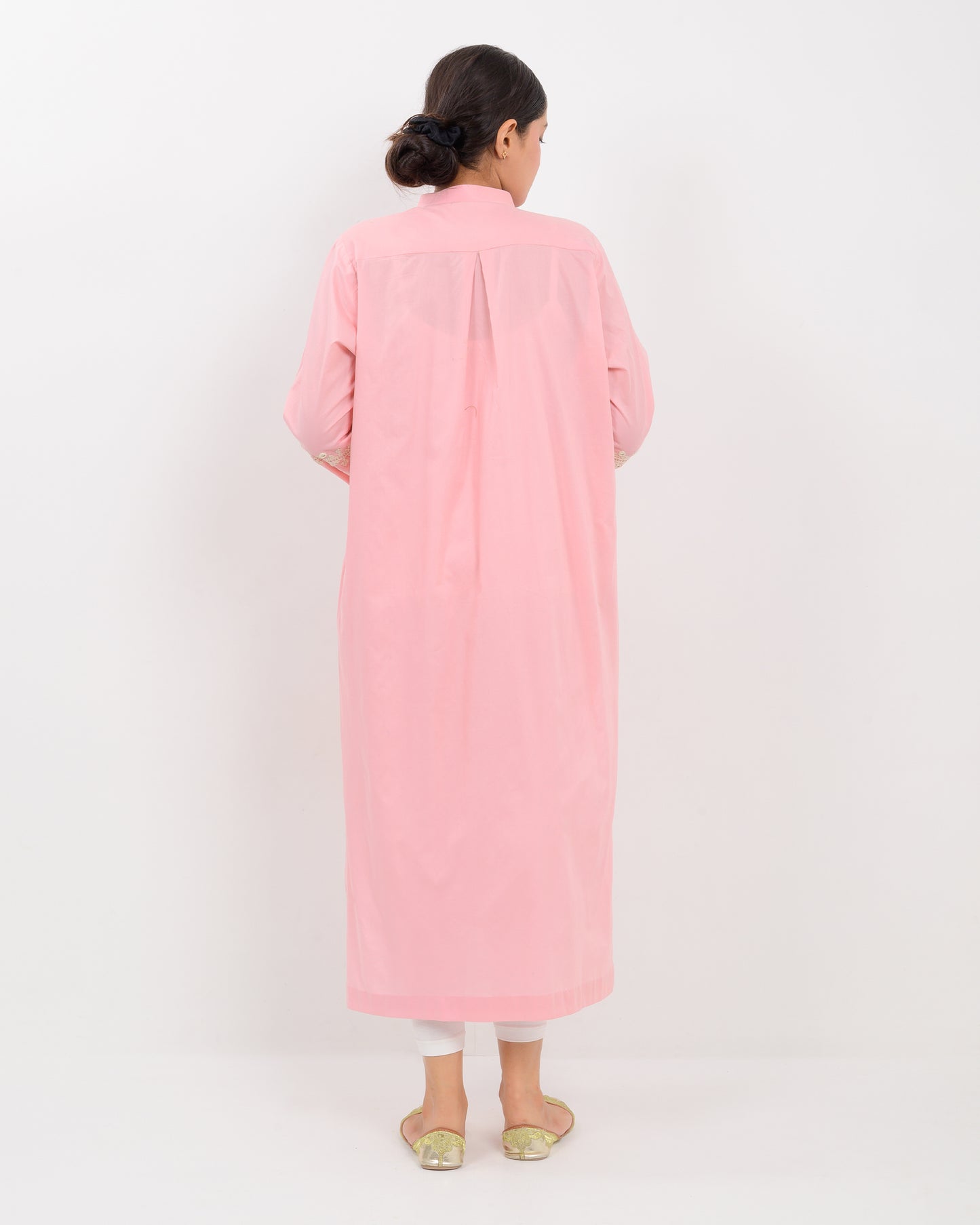 Woman wearing a pink cotton shirt with white embroidery on a white plan background