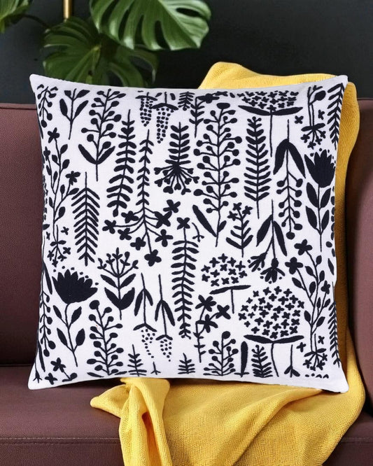 Decorative pillow with black floral pattern on white background, placed on a couch with yellow blanket.