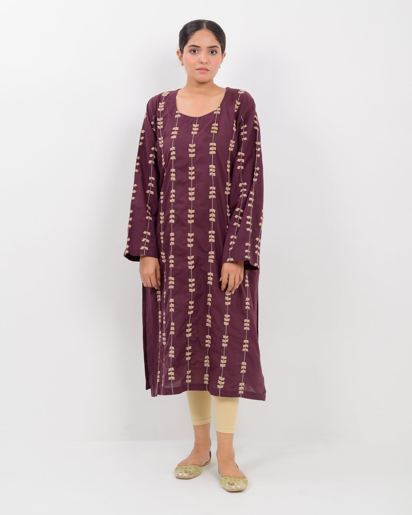 Woman wearing a maroon applique cutwork leaf-patterned shirt with beige pants on a white background