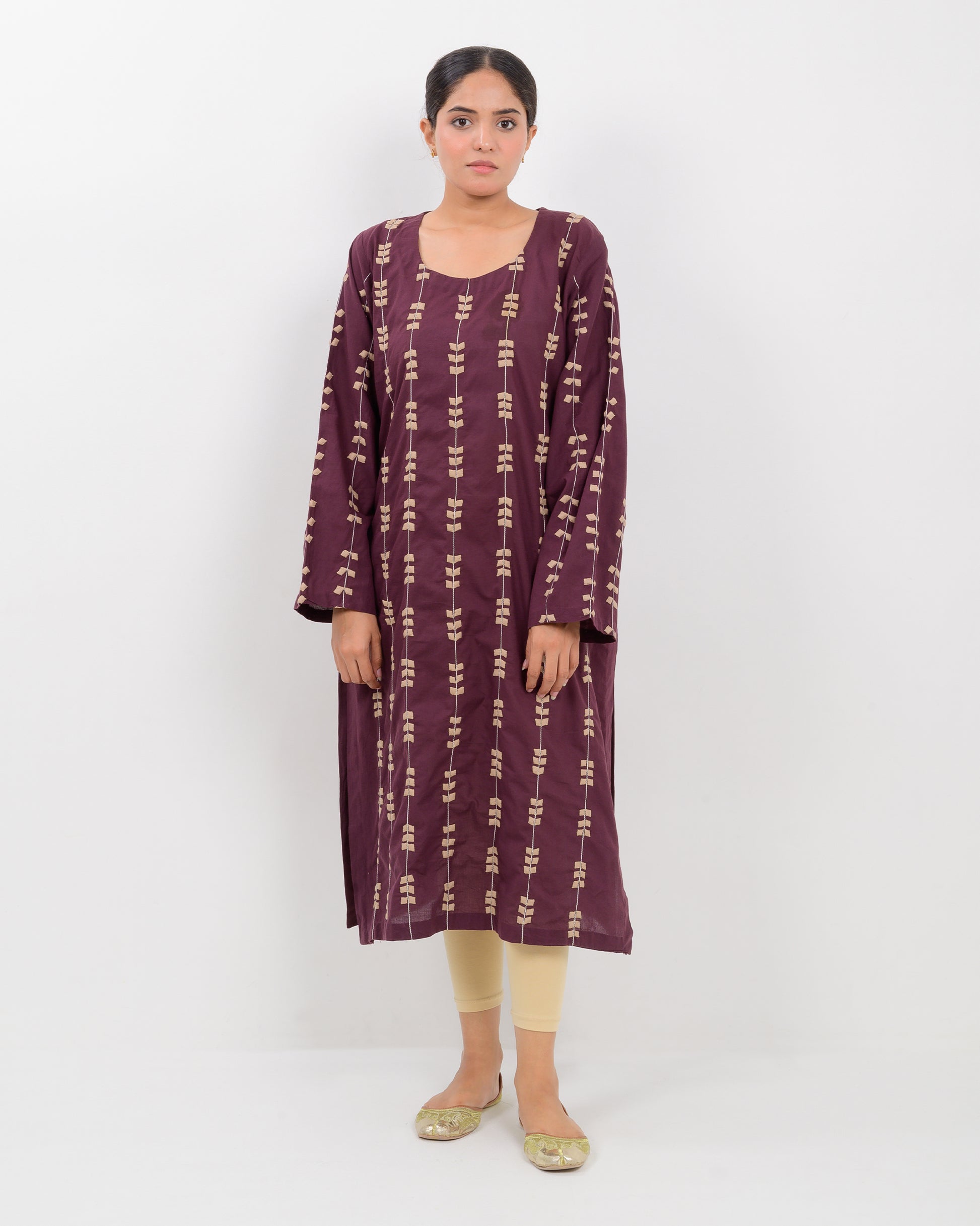Woman wearing a maroon applique cutwork leaf-patterned shirt with beige pants on a white background