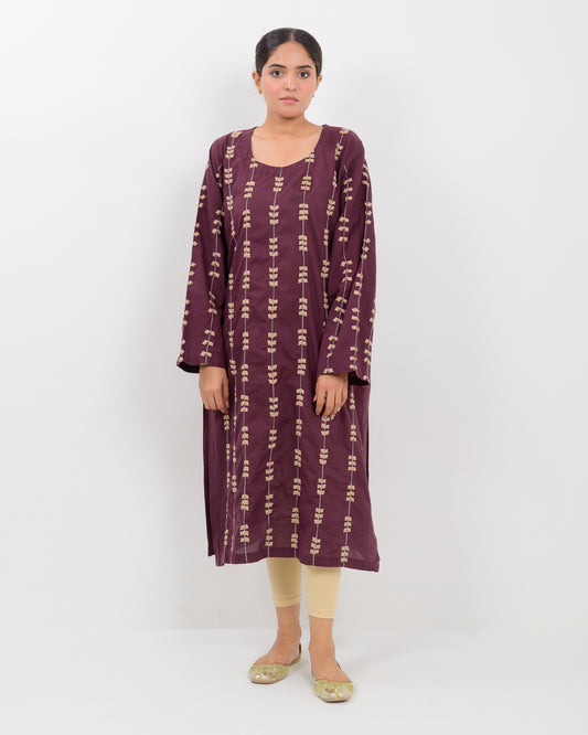Woman wearing a maroon applique cutwork leaf-patterned shirt with beige pants on a white background