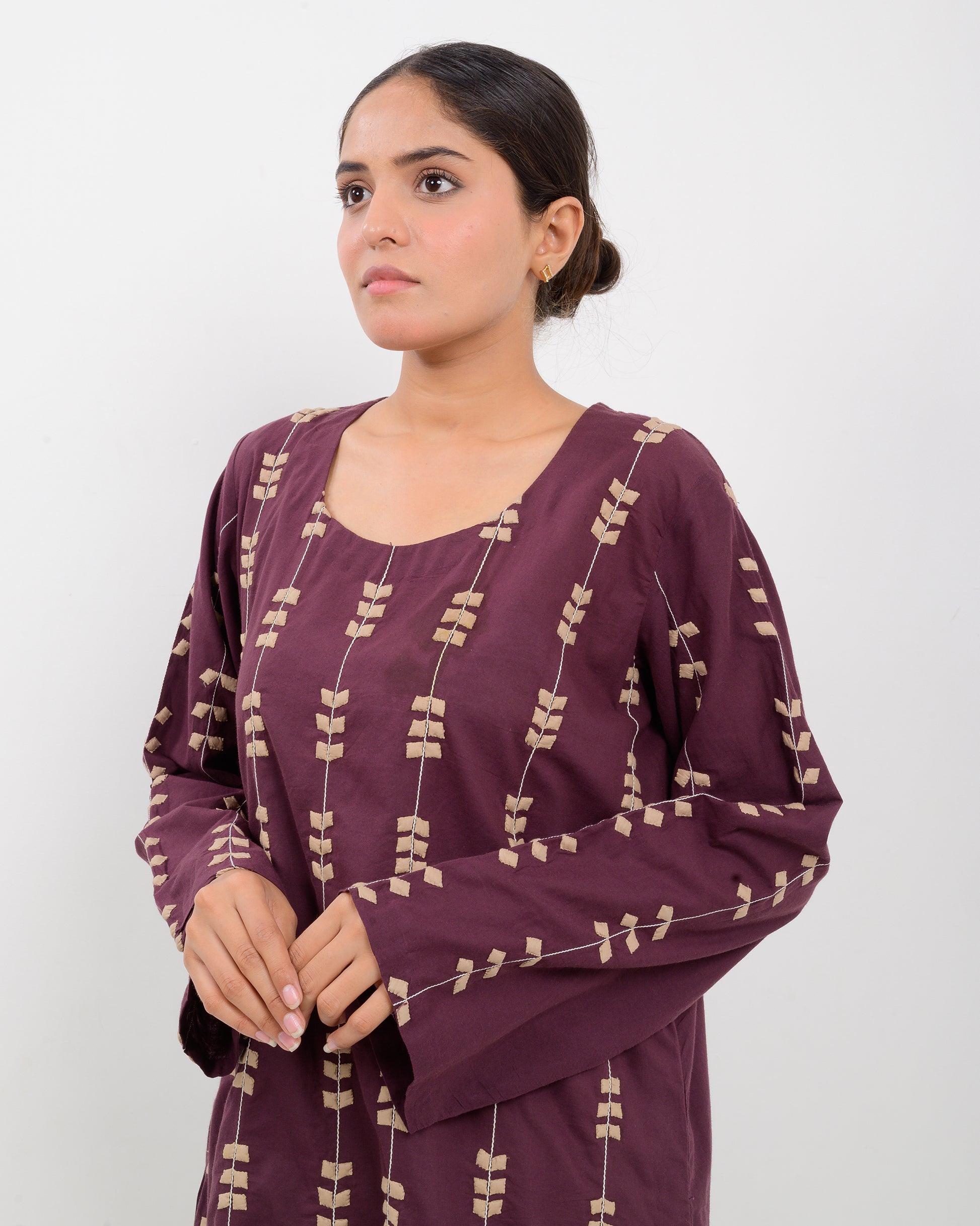Woman wearing a maroon applique cutwork leaf-patterned shirt with beige pants on a white background