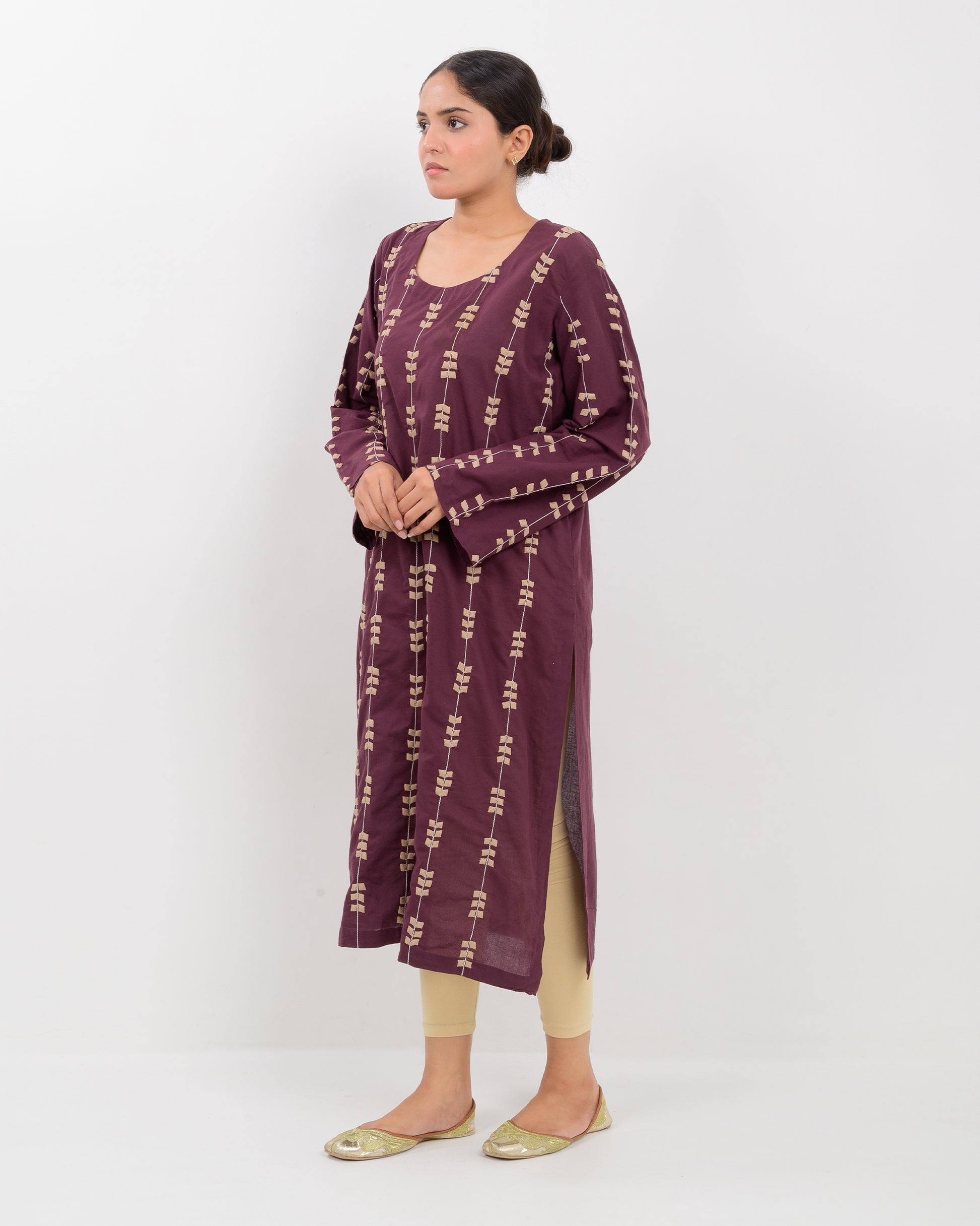 Woman wearing a maroon applique cutwork leaf-patterned shirt with beige pants on a white background