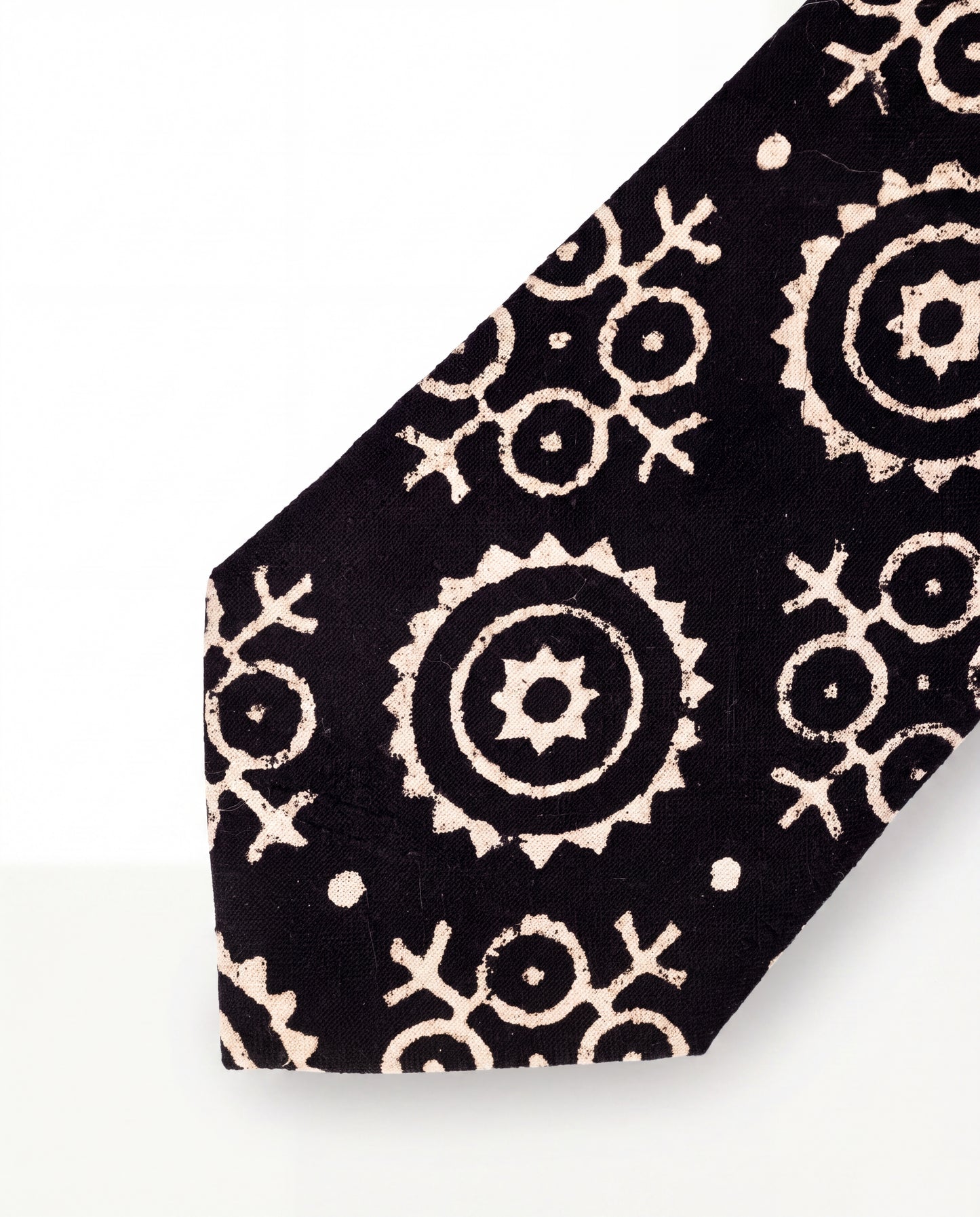 A close-up of a black necktie featuring a cream-colored distressed geometric and circular mandala pattern, set against a plain white background.
