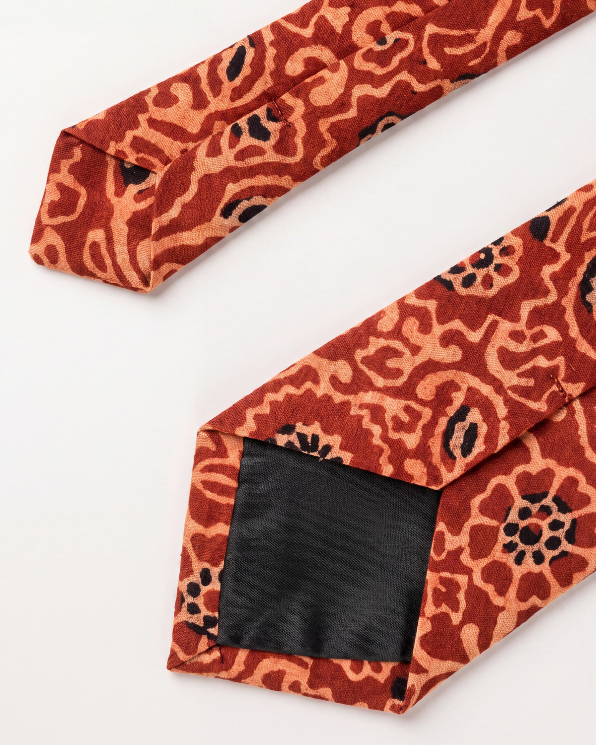 A close-up of a necktie with a rust-orange and beige abstract floral pattern, featuring a black satin inner band.