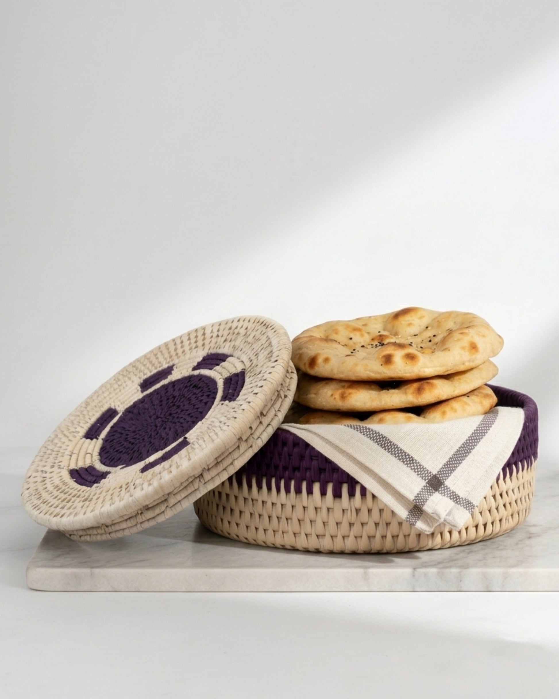 Woven basket with a lid and flatbreads on a white background