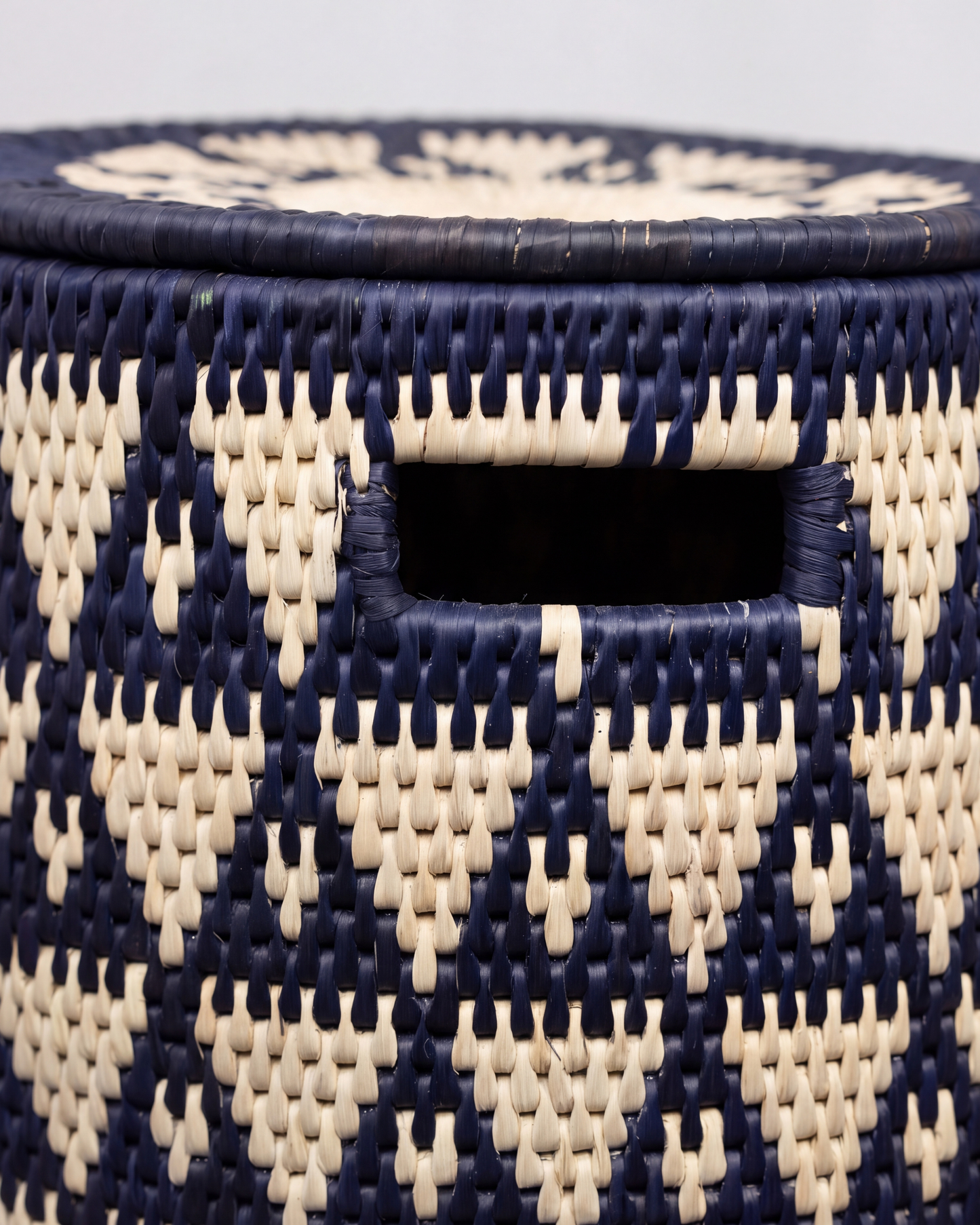 Close-up of a woven basket with a navy blue and natural beige geometric pattern, featuring a cutout handle.