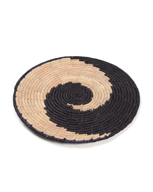 Round woven trivet with black and beige spiral design on a white background